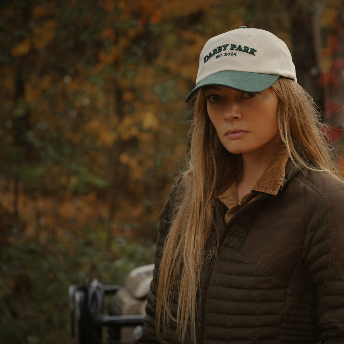 Woman wearing the cream Canvas Cap with a green brim and a quilted olive jacket in the fall woods.
