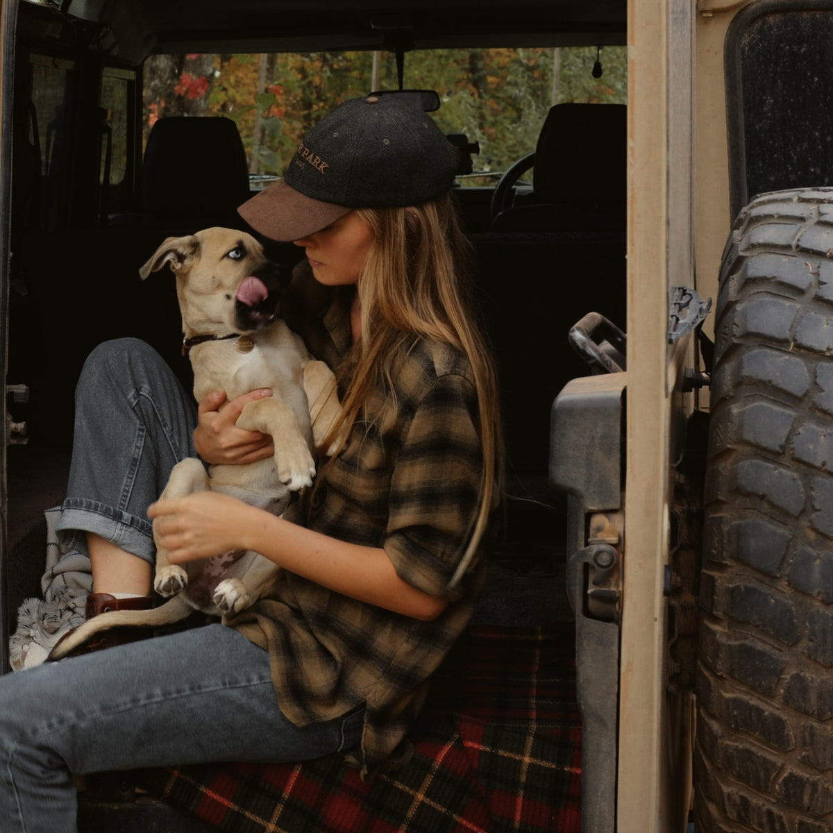 Woman in the Tweed Cap sitting in the back of a vintage truck with Winnie in her lap.